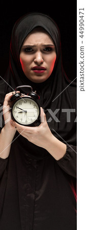 Portrait of beautiful serious scared frightened young muslim woman wearing black hijab holding alarm 44990471
