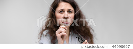 Young brunette girl with glasses. The girl put a magnifying glass to her lips. 44990697