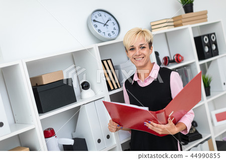 A young girl stands in the office with a red folder in her hands. 44990855