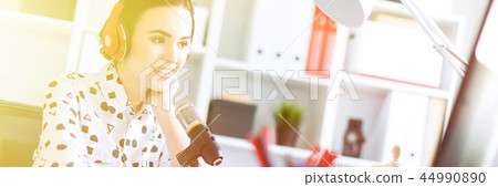 Beautiful young girl sitting in headphones and with microphone at table in office and talking. 44990890