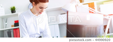 A young girl in the office is standing near the table, holding a pencil and a calculator in her hand 44990920