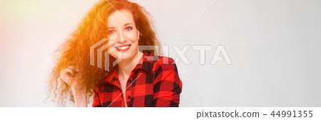 Young red-haired girl in a red checkered shirt. Young girl holds her hair with her hand 44991355