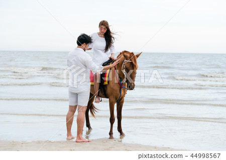 Young couple goes horse riding on tropical beach. Young couple goes horse riding on tropical beach. 44998567