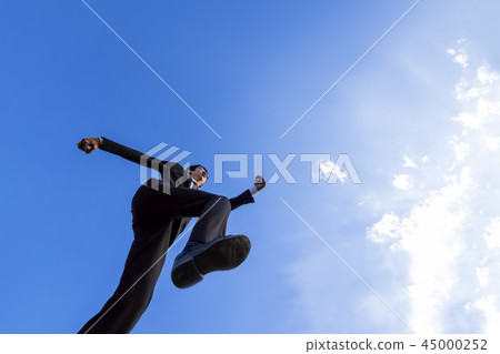 A young businessman in a suit who jumps against the blue sky. Energy, power, success, challenge image 45000252
