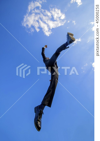 在跳躍反對藍天的衣服的一個年輕商人。能量,力量,成功,挑戰形象 在跳躍反對藍天的衣服的一個年輕商人。能量,力量,成功,挑戰形象 45000258