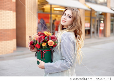 Caucasian fashion woman standing on the street near storefront shop windows holding flower-box with Caucasian fashion woman standing on the street near storefront shop windows holding flower-box with 45004981
