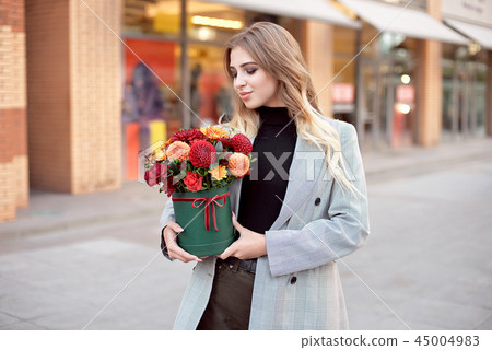 Caucasian fashion woman standing on the street near storefront shop windows holding flower-box with Caucasian fashion woman standing on the street near storefront shop windows holding flower-box with 45004983