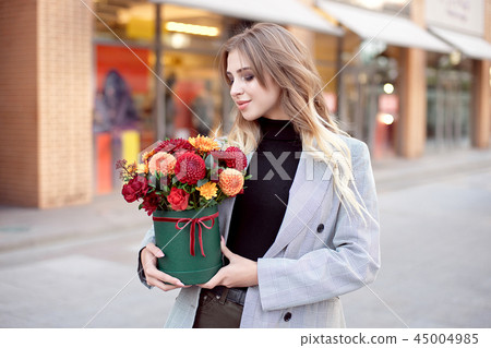 Caucasian fashion woman standing on the street near storefront shop windows holding flower-box with Caucasian fashion woman standing on the street near storefront shop windows holding flower-box with 45004985