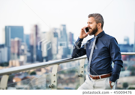 A portrait of businessman with smartphone standing against London view panorama. A portrait of businessman with smartphone standing against London view panorama. 45009476