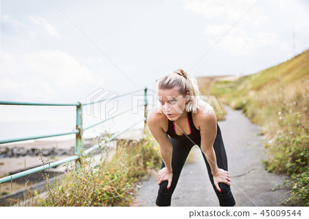 Young sporty woman runner in black activewear standing outside by the seaside, resting. Young sporty woman runner in black activewear standing outside by the seaside, resting. 45009544