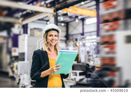A portrait of an industrial woman engineer in a factory, checking something. A portrait of an industrial woman engineer in a factory, checking something. 45009619