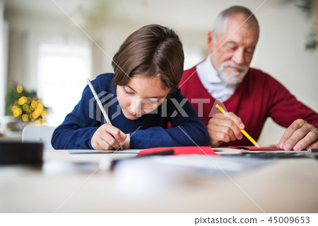 A small girl and her grandfather writing Christmas cards together. 45009653