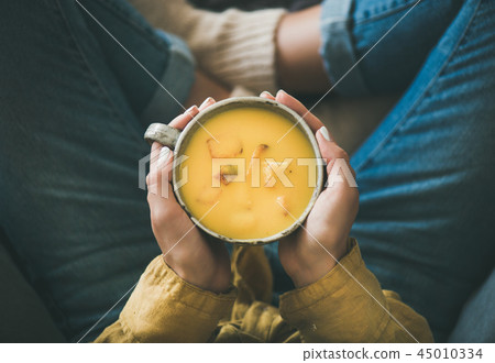 Female keeping mug of pumpkin yellow cream soup in hands 45010334