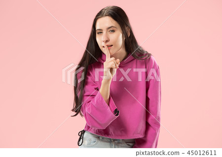 The young woman whispering a secret behind her hand over pink background The young woman whispering a secret behind her hand over pink background 45012611
