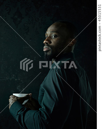 Stylish young black man with cup of coffee posing on dark background. Stylish young black man with cup of coffee posing on dark background. 45015531