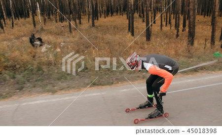 Training an athlete on the roller skaters. Biathlon ride on the roller skis with ski poles, in the 45018398