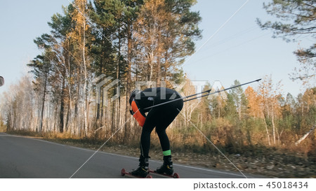 Training an athlete on the roller skaters. Biathlon ride on the roller skis with ski poles, in the Training an athlete on the roller skaters. Biathlon ride on the roller skis with ski poles, in the 45018434