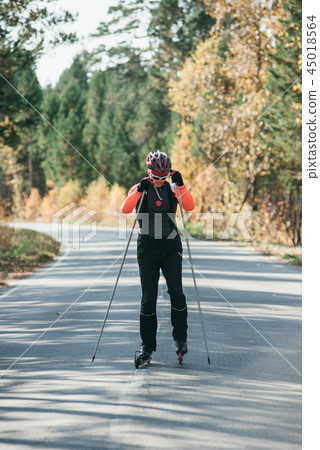 Training an athlete on the roller skaters. Biathlon ride on the roller skis with ski poles, in the Training an athlete on the roller skaters. Biathlon ride on the roller skis with ski poles, in the 45018564