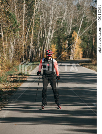 Training an athlete on the roller skaters. Biathlon ride on the roller skis with ski poles, in the 45018593