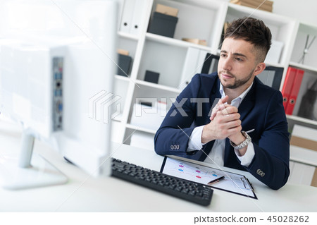 A young man sitting in the office at a computer Desk and working with documents. A young man sitting in the office at a computer Desk and working with documents. 45028262