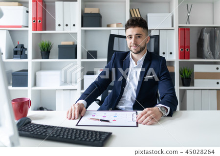 A young man sitting in the office at a computer Desk and working with documents. A young man sitting in the office at a computer Desk and working with documents. 45028264