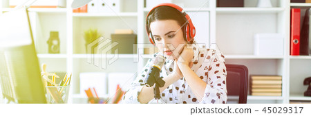 Beautiful young girl sitting in headphones and with microphone at table in office and talking. 45029317