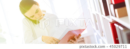 Young girl in the office near the rack and scrolls through the folder with the documents and speaks 45029711