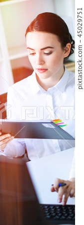 A young girl in the office holds a pen in her hand and works with documents and a computer. A young girl in the office holds a pen in her hand and works with documents and a computer. 45029751