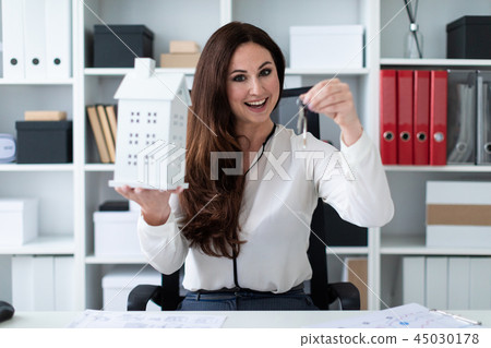 A young girl sitting at a table and holding a house and keys. A young girl sitting at a table and holding a house and keys. 45030178