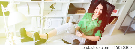 A young girl sits in the office, threw her legs on the table and holds the phone in her hands. 45030309