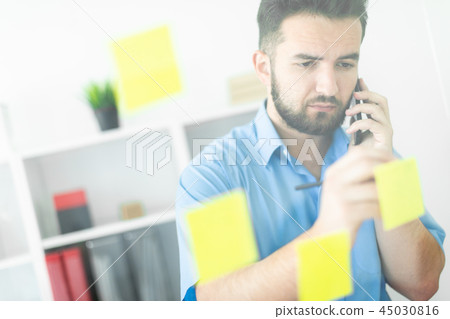 A young man stands in the office near a transparent Board with stickers. A young man stands in the office near a transparent Board with stickers. 45030816