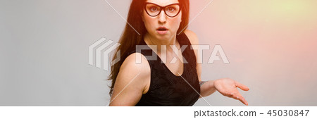 Portrait of emotional pretty confident puzzled astonished plus size model standing in studio on gray Portrait of emotional pretty confident puzzled astonished plus size model standing in studio on gray 45030847