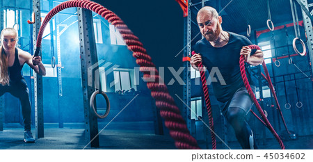 Man and woman with battle rope battle ropes exercise in the fitness gym. Man and woman with battle rope battle ropes exercise in the fitness gym. 45034602