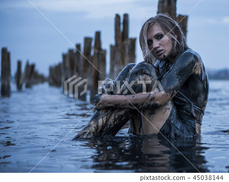 Portrait of Blonde Caucasian Girl Sitting Smeared in a Healthy Black Mud in old Firth with Wooden 45038144