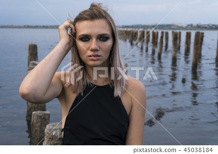 Portrait of Blonde Caucasian Girl in a Healthy Black Mud in old Firth with Wooden Posts for Salt Portrait of Blonde Caucasian Girl in a Healthy Black Mud in old Firth with Wooden Posts for Salt 45038184