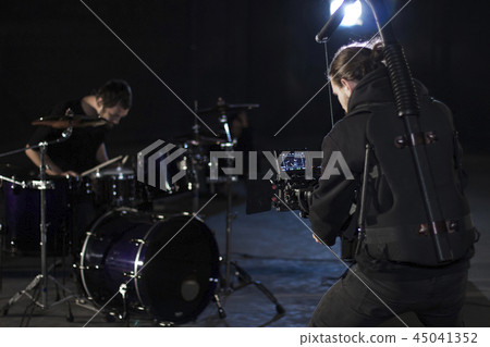 Professional videographer holding camera mounted on easy rig and filming a drummer. Videographer 45041352