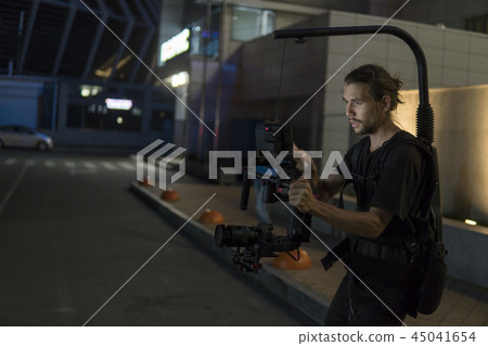Professional videographer holding camera on 3-axis gimbal which mounted on easy rig. Videographer Professional videographer holding camera on 3-axis gimbal which mounted on easy rig. Videographer 45041654