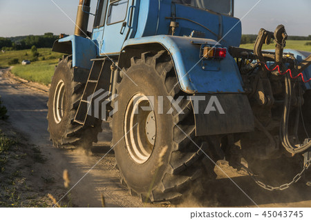 A blue tractor rides along a road in a wheat field. A blue tractor rides along a road in a wheat field. 45043745