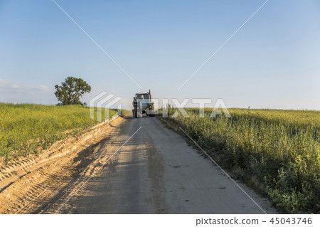 A blue tractor rides along a road in a wheat field. A blue tractor rides along a road in a wheat field. 45043746