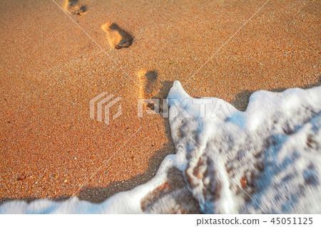 Footstep on red sand leadind into the water, blurred fast sea surf Footstep on red sand leadind into the water, blurred fast sea surf 45051125