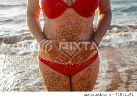 Women in red bikini with her hands on belly with sea waves on background 45051141