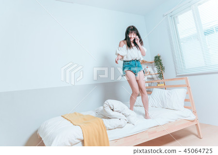甜美可愛亞洲女孩拿著手機聽音樂在床上開心笑著跳舞 45064725