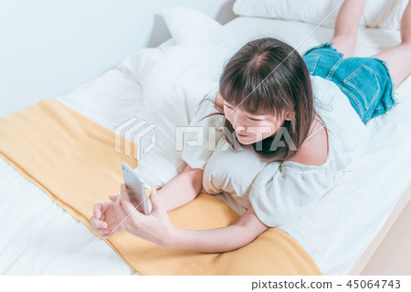 甜美可愛亞洲女孩在床上笑著開心拿著手機自拍視訊聊天 45064743