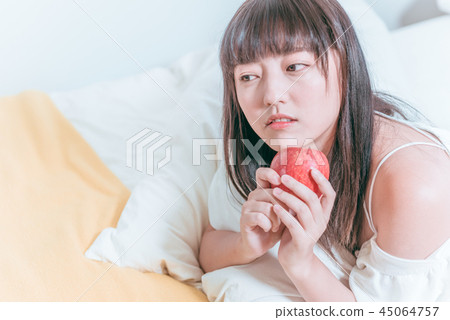 Sweet cute asian girl holding apple in bed thoughtfully Sweet cute asian girl holding apple in bed thoughtfully 45064757
