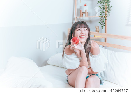 Sweet cute asian girl sitting on bed happy smiling holding apple ready to eat Sweet cute asian girl sitting on bed happy smiling holding apple ready to eat 45064767