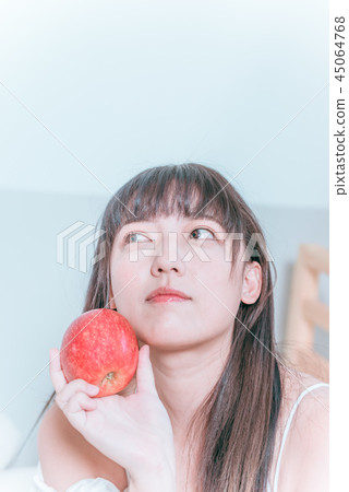 Sweet cute asian girl sitting on bed happy smiling holding apple ready to eat 45064768