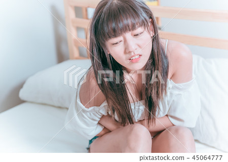 甜美可愛亞洲女孩坐在床上痛苦難過抱著肚子不舒服生病 45064777