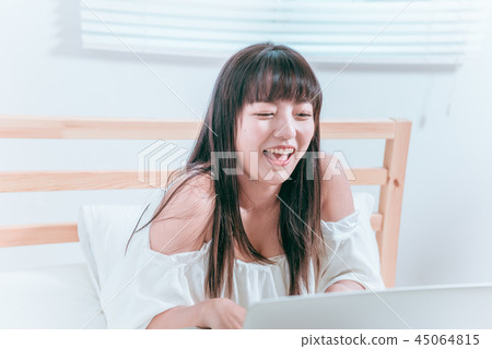甜美可愛亞洲女孩坐在床邊開心笑著使用筆記型電腦視訊聊天逛網站 45064815