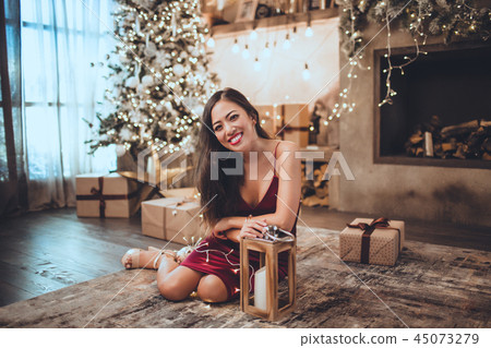 Young beautiful asian girl is fashion red dress sitting at home near christmas tree in cozy interior Young beautiful asian girl is fashion red dress sitting at home near christmas tree in cozy interior 45073279