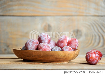 ripe plums in wooden plate on wooden background 45075679